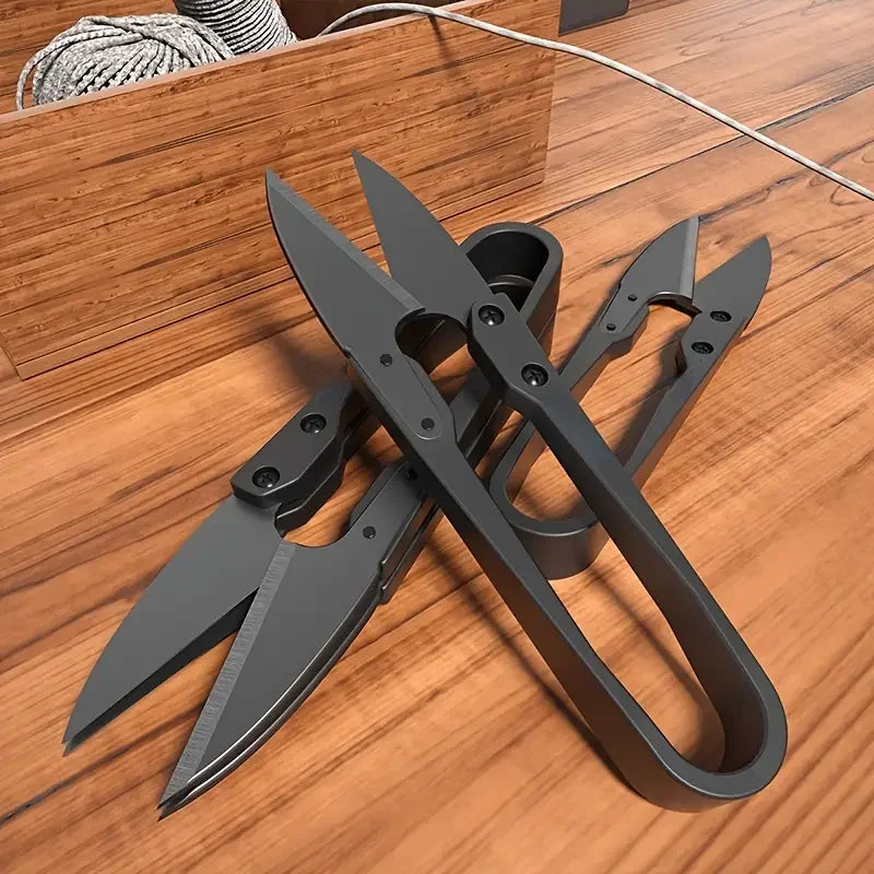 Trois ciseaux coupe-fil de couture noirs en métal empilés sur une surface en bois