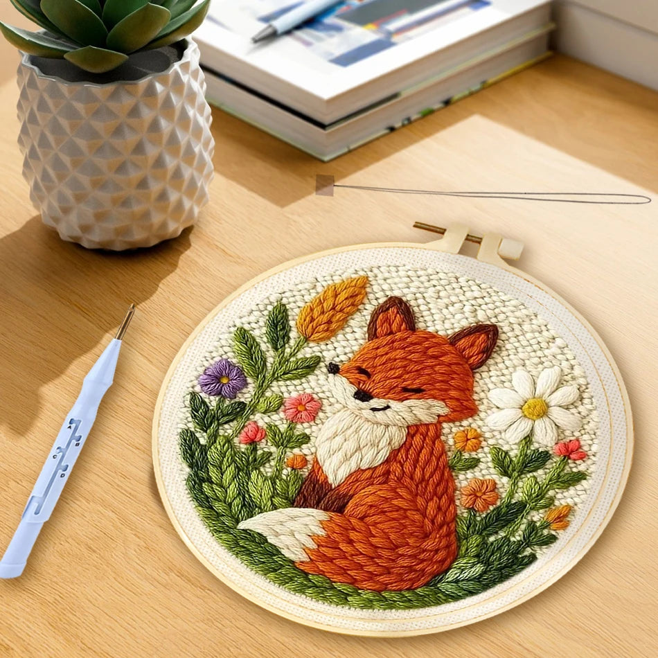 Cadre rond fini en broderie punch needle représentant un renard roux assis au milieu de fleurs sauvages et de marguerites.