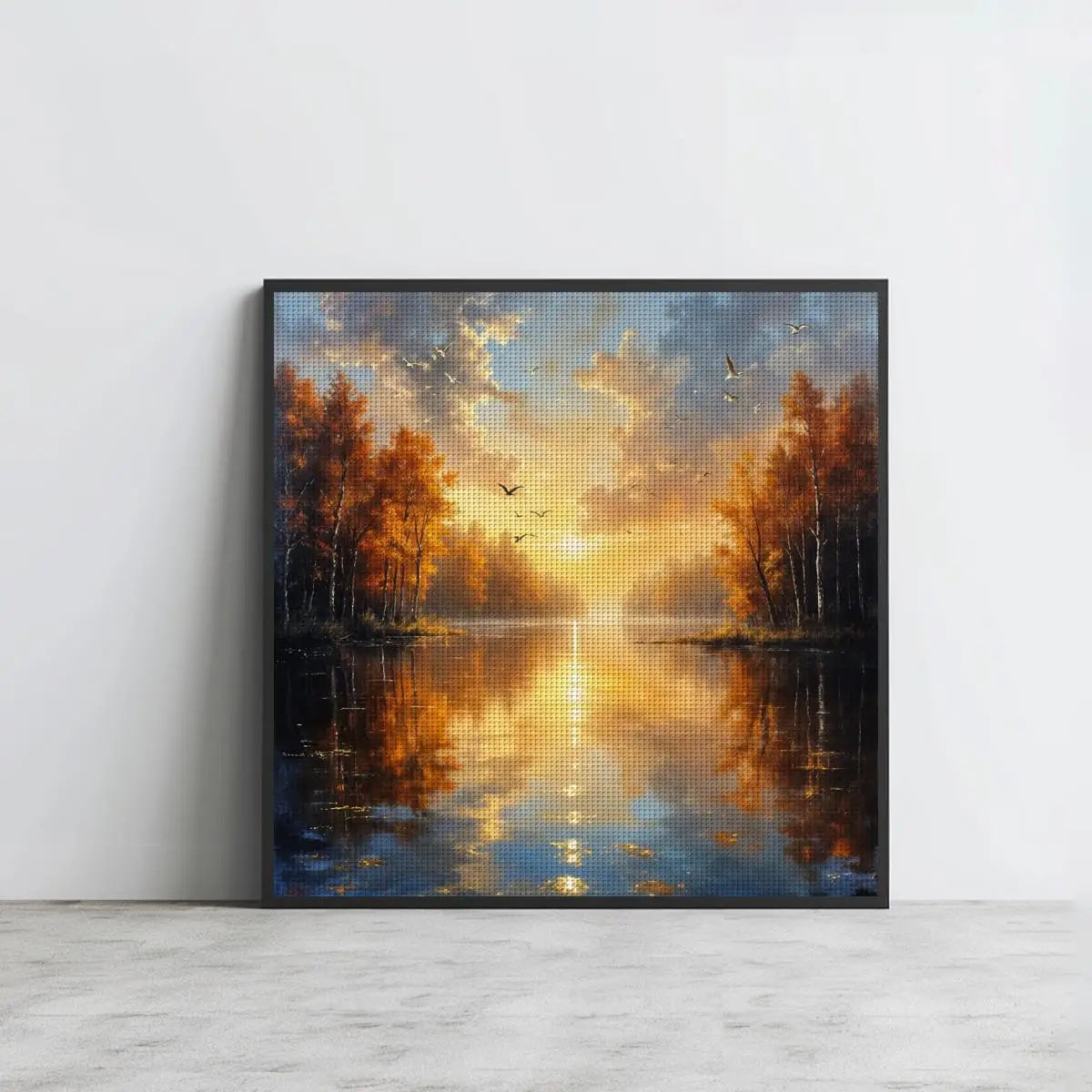 Grand tableau en point de croix paysage de forêt d'automne encadré en noir et posé sur un sol en parquet blanc.