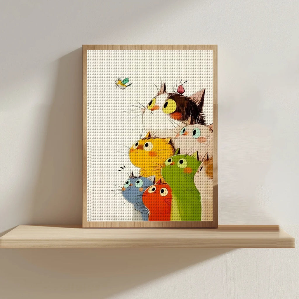 Tableau broderie fait main avec motif de chats amusants encadré en bois clair et posé sur une étagère flottante.