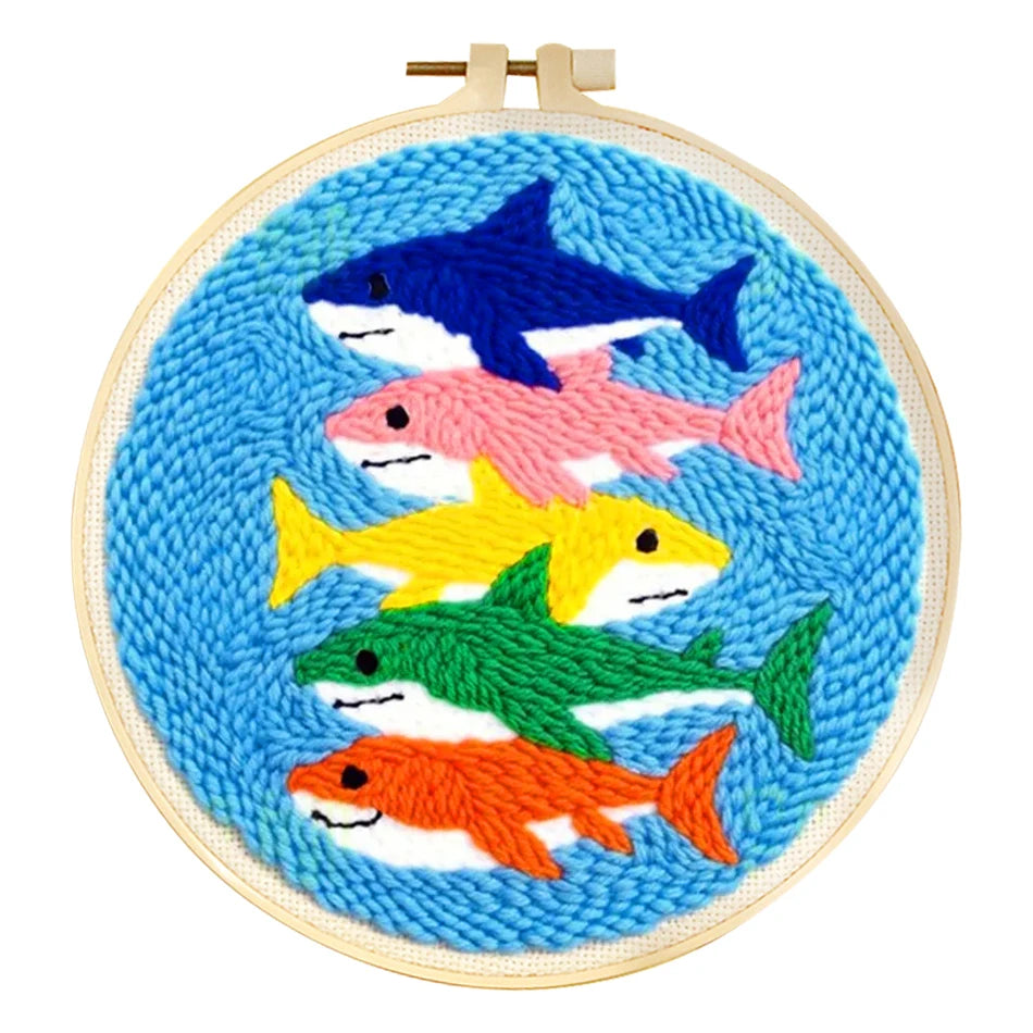 Canevas de broderie punch needle pour débutant illustrant une superposition de cinq requins colorés rigolos sur un fond bleu ciel.