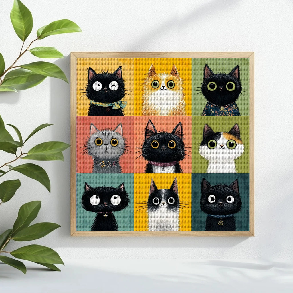 Tableau broderie fait main carre avec motif de chats rigolos encadre en bois clair et pose sur un meuble a cote d'une plante verte.