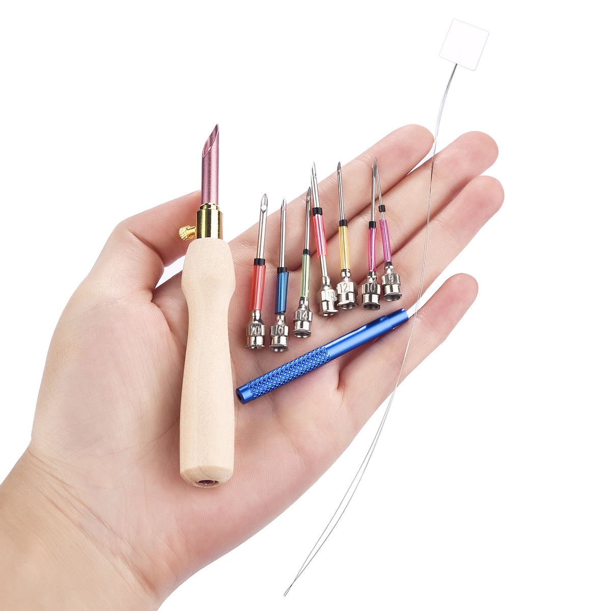 Une main tenant un manche en bois pour punch needle entouré de plusieurs pointes en métal de tailles différentes et d'un enfile-aiguille long.