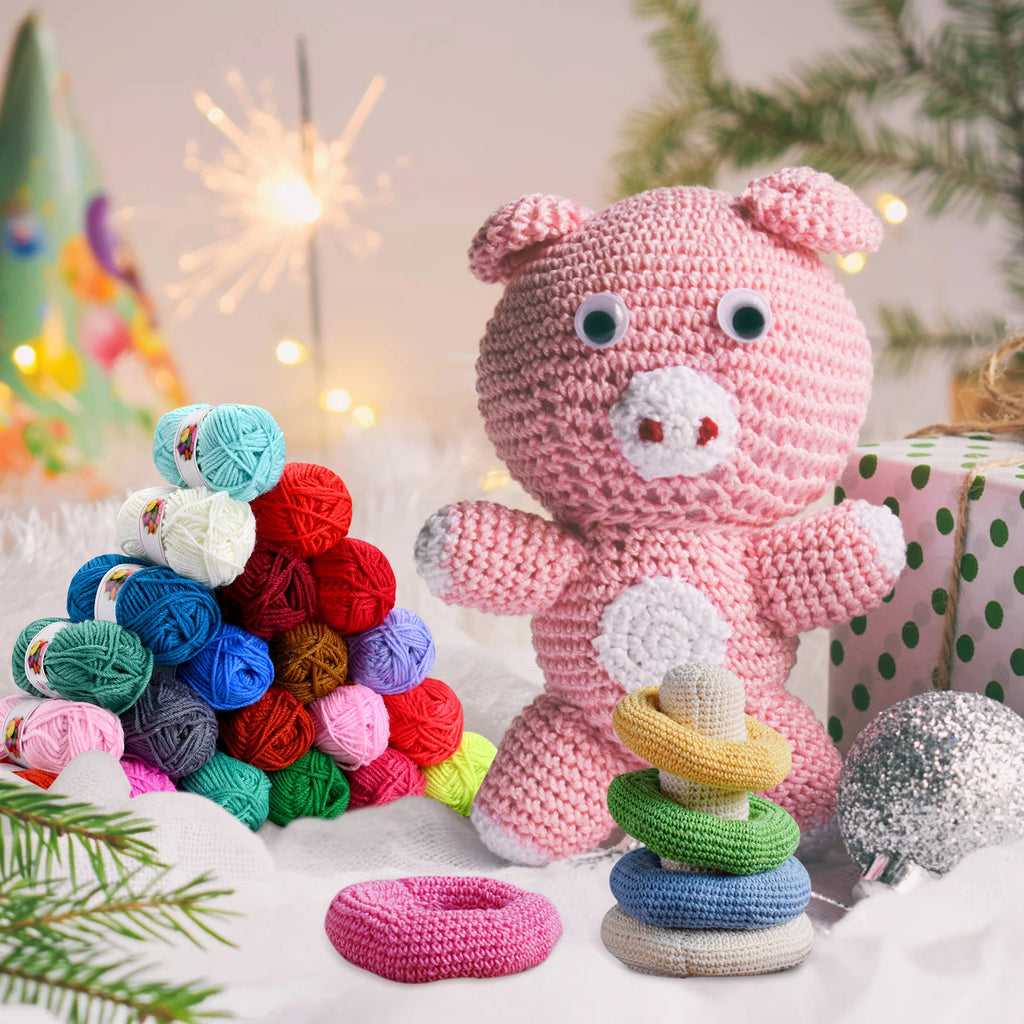 Peluches en laine faites main dont un cochon rose au crochet à côté d'une pile de mini pelotes