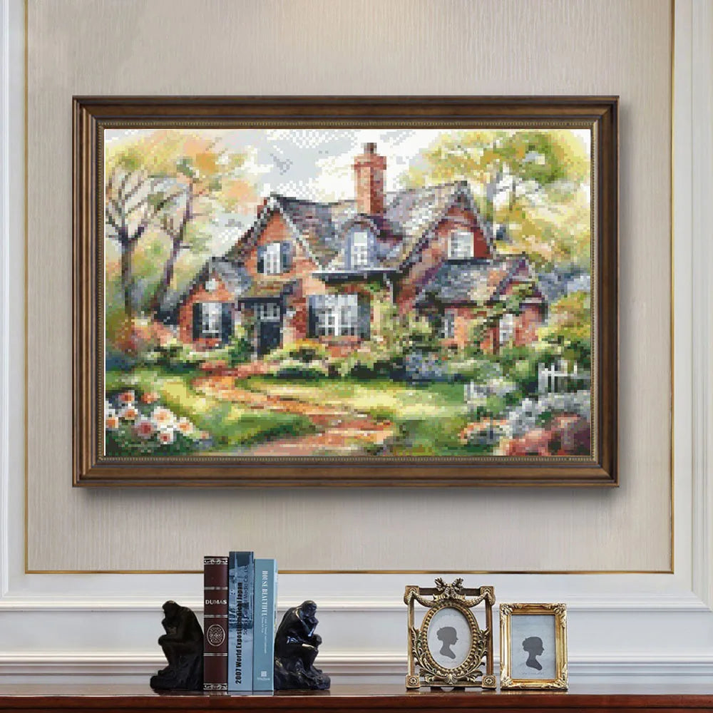 Broderie paysage de maison de campagne champêtre encadrée en bois marron posée sur un buffet chic.