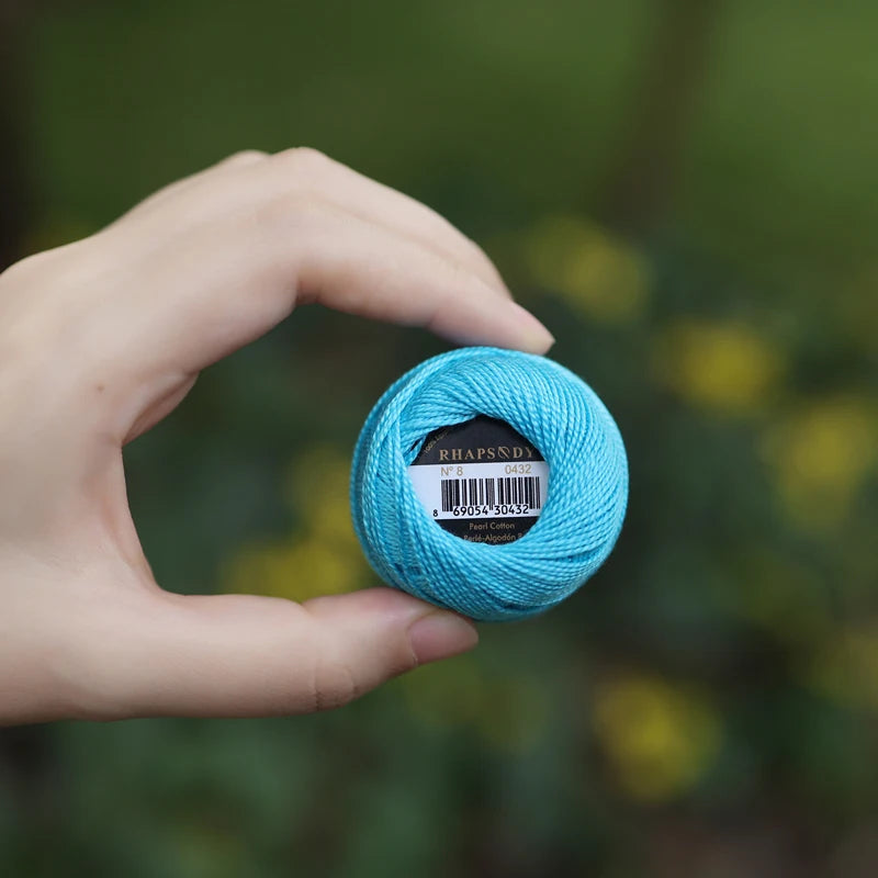 Une main tenant une petite pelote de coton perlé de couleur bleu turquoise vif.