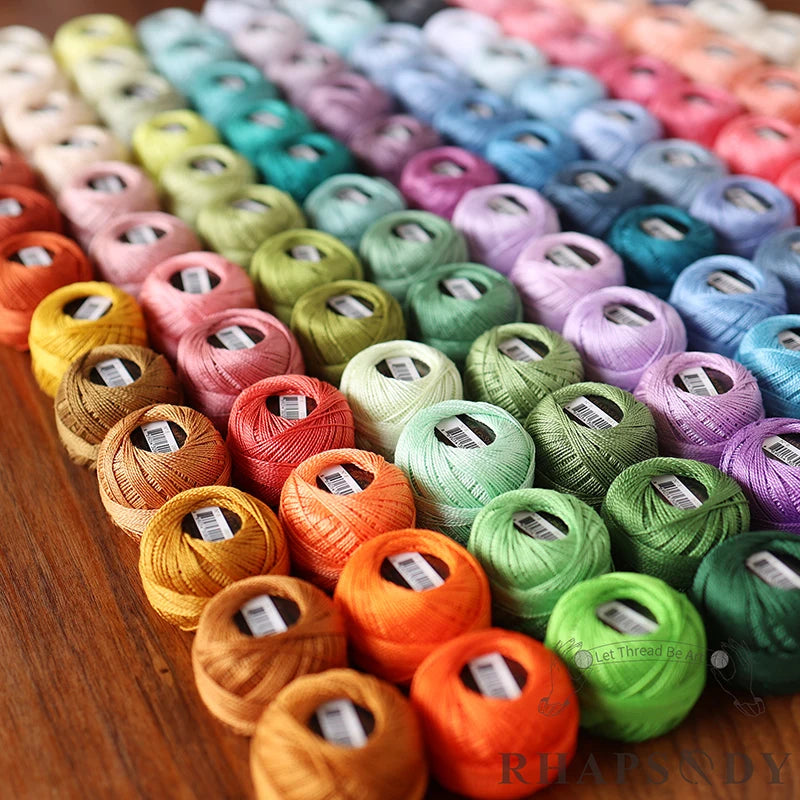 Grand assortiment multicolore de pelotes de coton perlé pour la broderie et le crochet, disposées en lignes par nuances de couleurs.