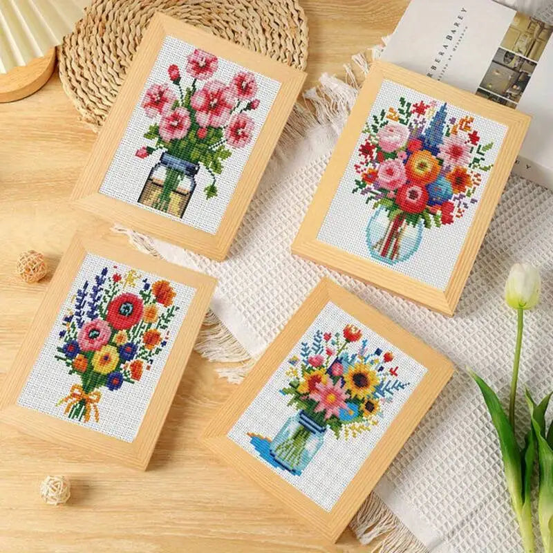 Collection de quatre petits tableaux de fleurs en point de croix encadres dans des cadres en bois clair disposes sur une table de decoration.