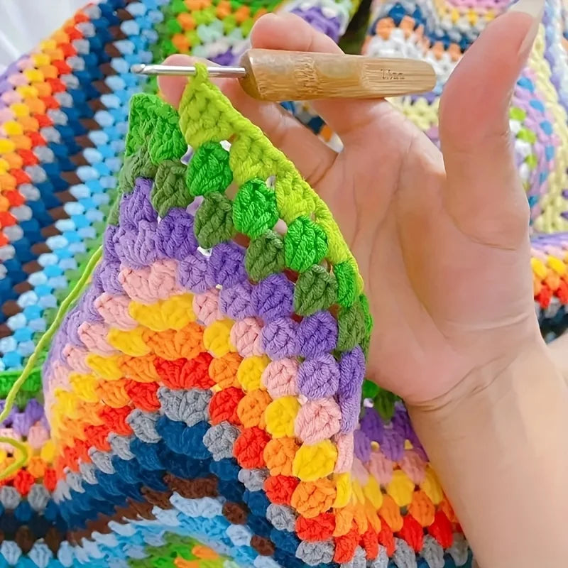 Main utilisant un crochet en bois pour assembler un plaid multicolore en laine avec des points serrés