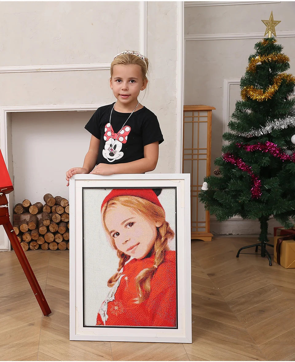 Petite fille tenant un grand cadre avec un portrait brodé personnalisé fait main en point de croix dans un salon.