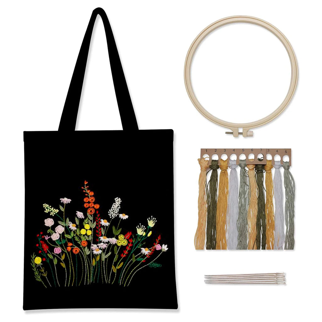 Kit complet de broderie pour débutant comprenant un tote bag en toile noire imprimé de fleurs sauvages colorées, un tambour en bois, des fils moulinés et des aiguilles.
