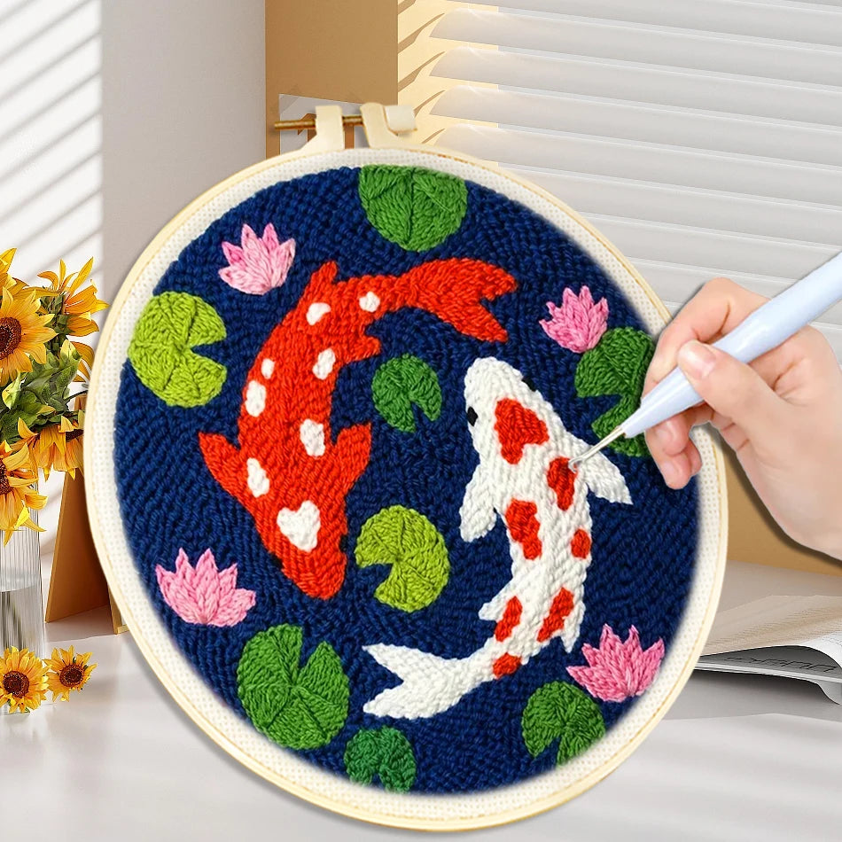Main utilisant une aiguille magique punch needle pour broder un motif de carpes koi japonaises rutilantes dans un tambour en bois sur fond de bureau.