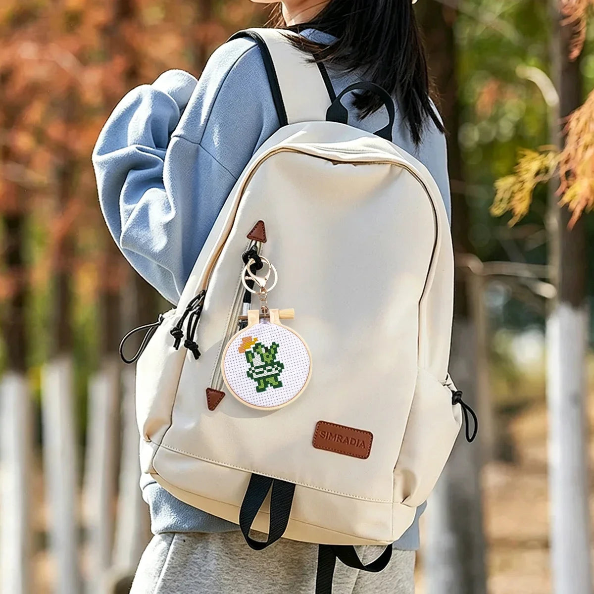 Mini tambour de broderie fait main dinosaure vert utilise comme porte-cle decoratif et accroche sur la fermeture d'un sac a dos blanc.