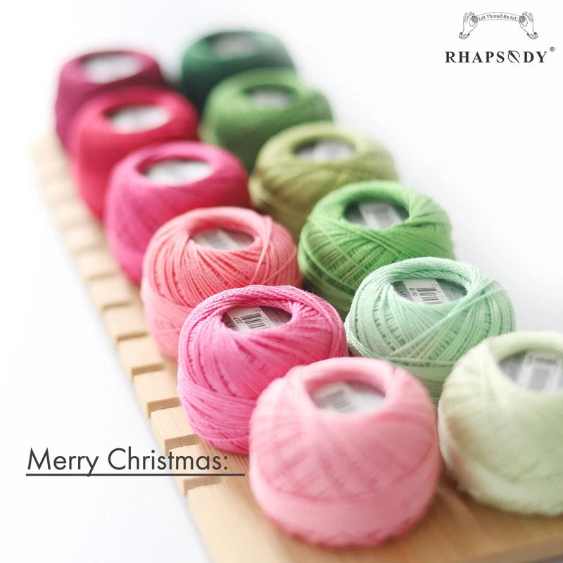  Assortiment de petites pelotes de fil à broder roses et vertes disposées sur un support en bois clair.
