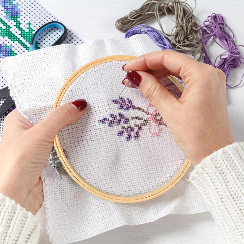 Mains d'une brodeuse en train de réaliser un motif floral violet sur un tissu blanc tendu